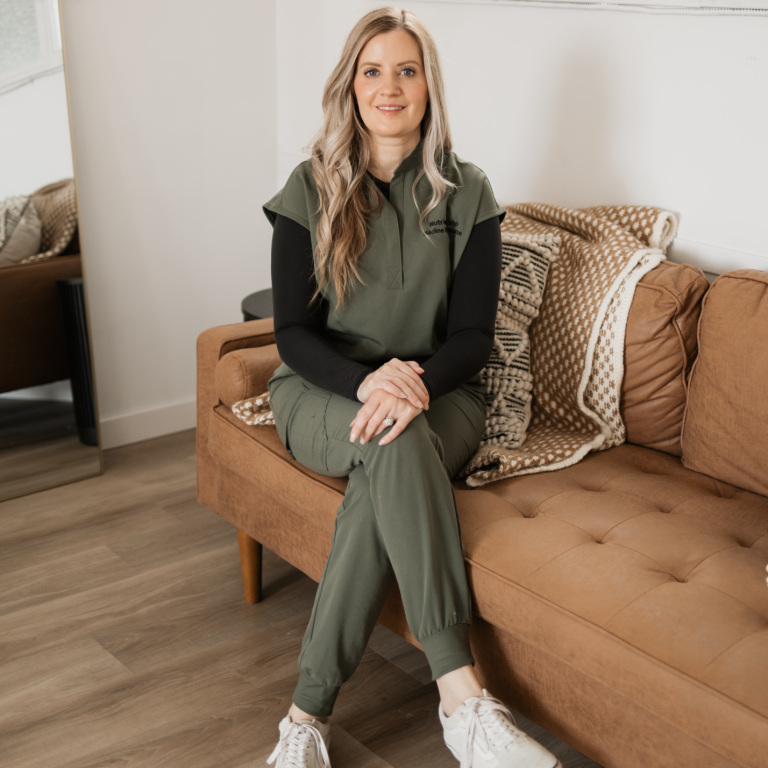 Nadine sitting on a couch, wearing green scrubs and white sneakers, in a bright room.